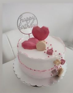 a white cake with pink frosting and hearts on top, sitting on a table