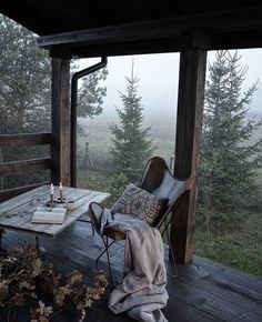 a wooden porch with a table and chairs on it, overlooking the trees in the fog