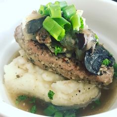 a white plate topped with mashed potatoes and meat covered in mushrooms, celery