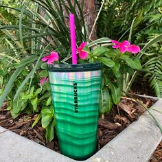 there is a green cup with pink flowers in the planter next to some plants