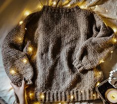 a woman's sweater with lights around it on top of a bed next to a candle