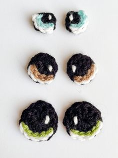 four crocheted black and green buttons on a white surface