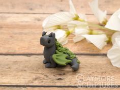 a small gray cat figurine sitting on top of a wooden table next to white flowers