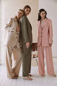 three women standing next to each other in suits and sandals, one wearing a pink blazer