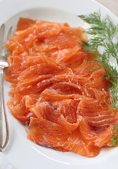 a white plate topped with sliced salmon next to a fork