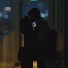 two people standing next to each other in front of a window with city lights behind them