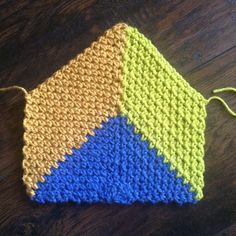 a crocheted dishcloth on a wooden table with yarn in the shape of a triangle