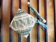 an origami graduation cap and one dollar bill on top of a wooden wall