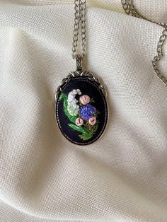 a necklace with flowers on it sitting on a white cloth background, hanging from a chain