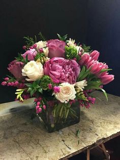 a glass vase filled with pink and white flowers on top of a marble countertop