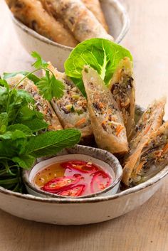 a bowl filled with different types of food on top of a wooden table next to dipping sauce