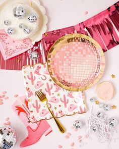 a table topped with pink and white plates and confetti covered napkins next to a cake