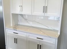 a kitchen with white cabinets and marble counter tops