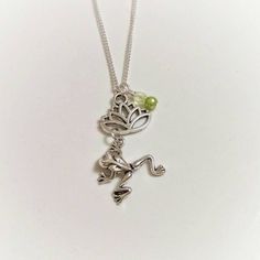 a silver necklace with a frog on it's back and a green bead in the middle