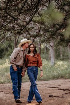 a man and woman are walking through the woods with their heads close to each other