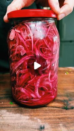 a person holding a jar with red liquid in it on top of a wooden table