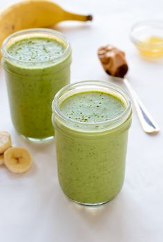 two glasses filled with green smoothie next to bananas