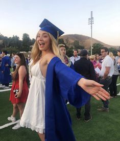 a woman in a graduation cap and gown holding her hand out to the side with other people standing around