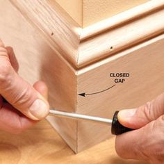 a person using a screwdriver to fix a wooden cabinet door gap with the help of a woodworking tool