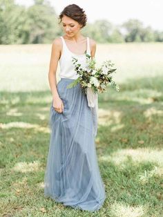 a woman standing in the grass holding a bouquet