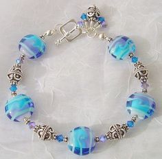 "This is a bracelet I designed using beautiful lampwork (handmade artisan glass) from a talented artist here on Ebay, 4mm 2X AB tanzanite bi-cone swarovski crystals, 4mm capri blue bi-cone swarovski crystals, and bali sterling silver. If wanted, I will happily adjust the size, or change the clasp to a desired clasp, at no extra charge. It currently fits a 7\" wrist and is strung on 49 strand wire with a sterling toggle clasp. Your jewelry will come to you in a beautiful gift box." Fusion Style Czech Glass Jewelry Gift, Fusion Style Czech Glass Jewelry For Gifts, Czech Glass Bracelet With Unique Variations, Spiritual Czech Glass Crystal Bracelet As Gift, Nickel-free Czech Glass Bracelets With Round Beads, Unique Design Czech Glass Bracelets As A Gift, Blue Bracelets With Unique Round Beads, Czech Glass Bracelets With Spacer Beads For Gifts, Czech Glass Bracelets With Spacer Beads As Gift