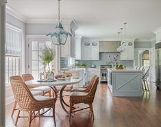 a kitchen with white cabinets and wood flooring next to a dining room table surrounded by wicker chairs