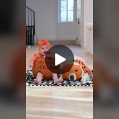 a baby sitting on the floor next to a dog wearing a pumpkin costume and holding a sign that says my first halloween