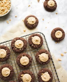 chocolate cookies with peanut butter frosting on a cooling rack next to a bowl of peanuts