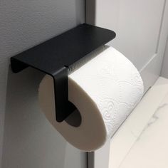 a roll of toilet paper is hanging from a black shelf on the wall next to a white door