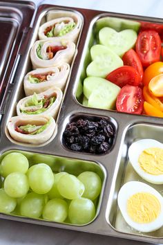 an assortment of fruits and vegetables in a metal tray with eggs, tomatoes, cucumbers, and other foodstuffs