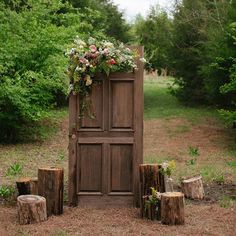 a wooden gate with flowers on it surrounded by trees and stumps in the woods