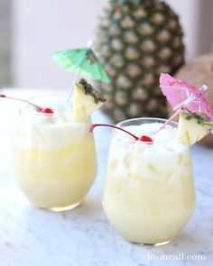 two glasses filled with drinks sitting on top of a table next to a pineapple