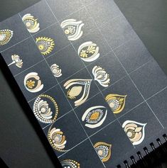 a spiral notebook with gold and silver designs on black paper next to a cell phone