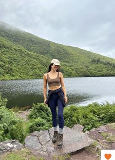 a woman standing on top of a rock next to a lake