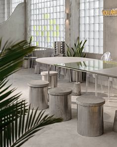 an indoor dining area with tables, stools and plants in the center surrounded by large windows