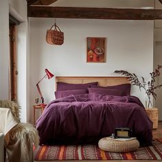 a bed with purple sheets and pillows in a room next to a rug on the floor