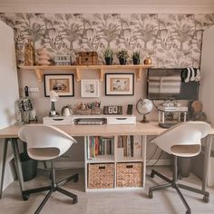 two white chairs sitting in front of a desk with bookshelves and pictures on the wall