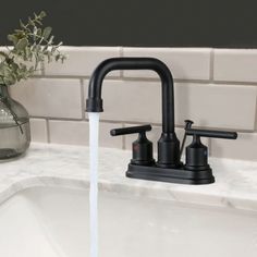 a black faucet with water running from it in a sink next to a vase