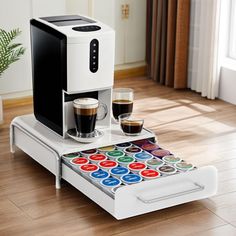 a white coffee maker sitting on top of a wooden table next to two cups of coffee