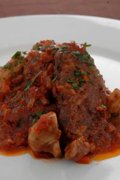 a white plate topped with meat covered in sauce and garnished with parsley