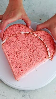 two hands holding a heart shaped cake on a plate