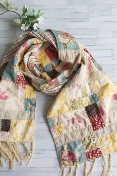 a multicolored patchwork scarf with fringes and flowers sitting on a white brick wall