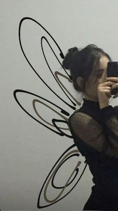 a woman taking a selfie in front of a wall with an angel wings design on it