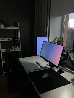 two computer monitors sitting on top of a desk in front of a window with a view of the city