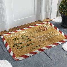 a welcome mat on the floor in front of a door with a christmas tree and potted plant