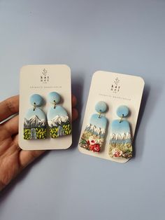 pair of earrings with mountain scene on them being held in front of each other by a card