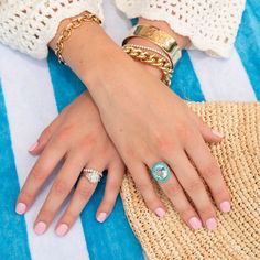 a woman's hands with rings and bracelets on top of a straw bag