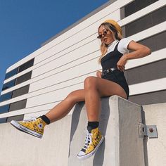 a woman sitting on top of a cement block wearing yellow and black converse shoes with her legs crossed