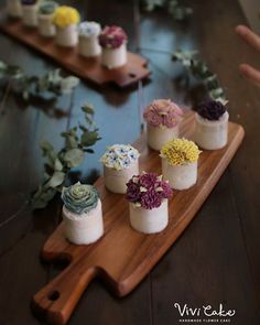 there are many small cupcakes with flowers on the wooden platter next to each other