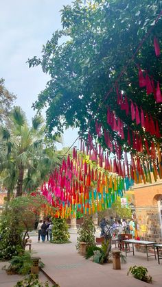 many colorful streamers hanging from trees in a courtyard area with people walking around them